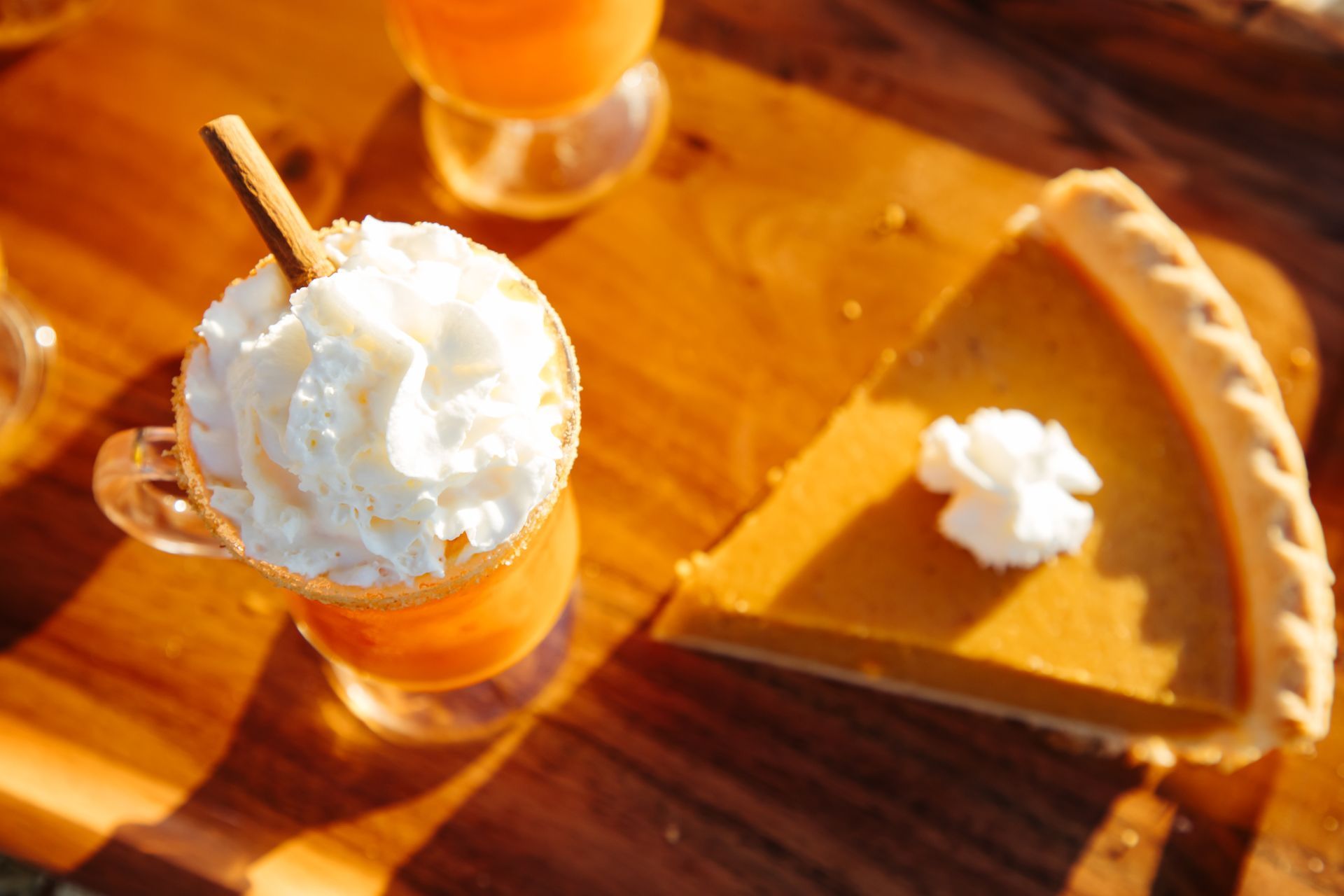 A slice of pumpkin pie and a cup of whipped cream on a wooden table.