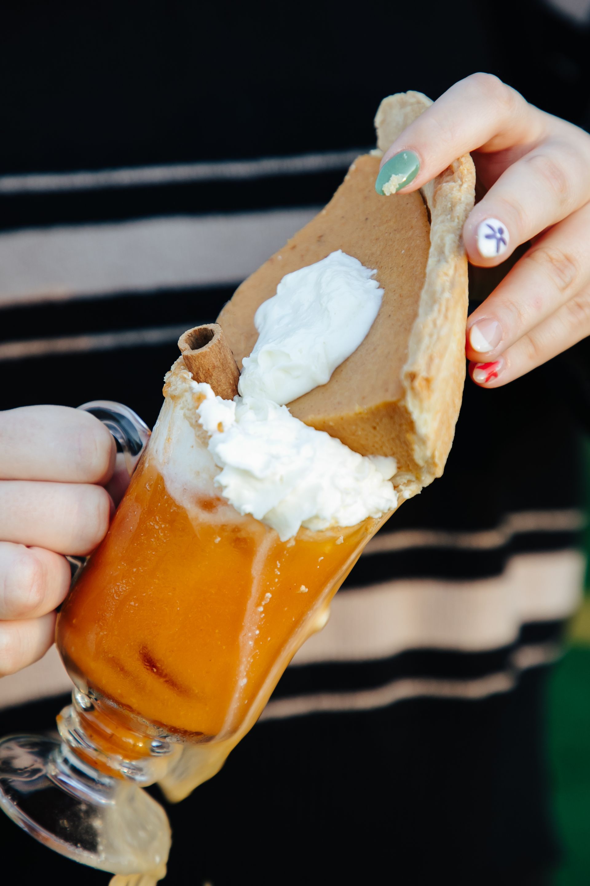 A person is holding a glass of pumpkin pie with whipped cream on top.