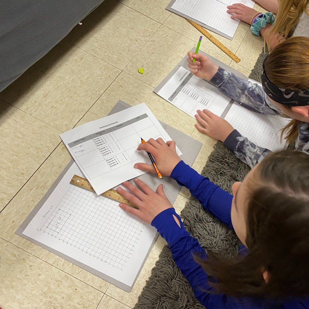 A group of children are sitting at a table with papers and pencils