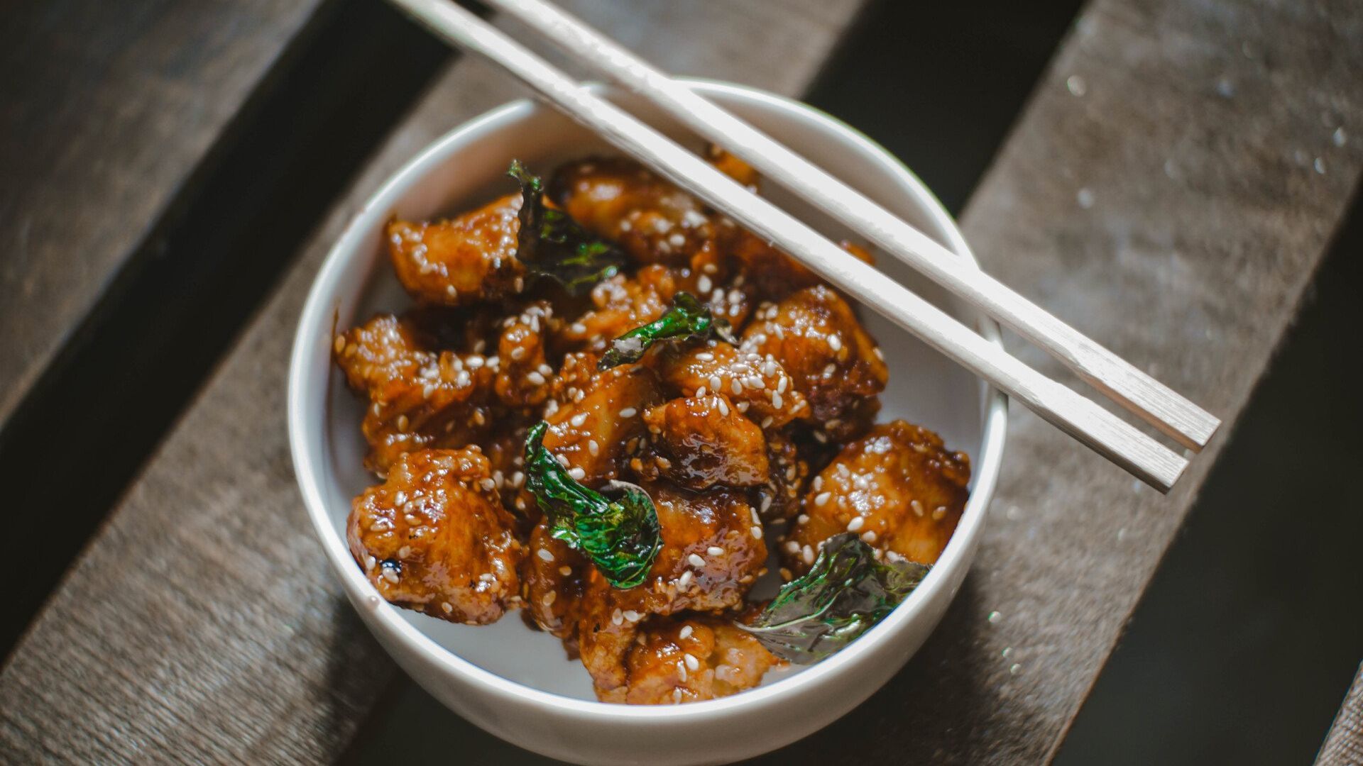 A bowl of food with chopsticks on a wooden table.
