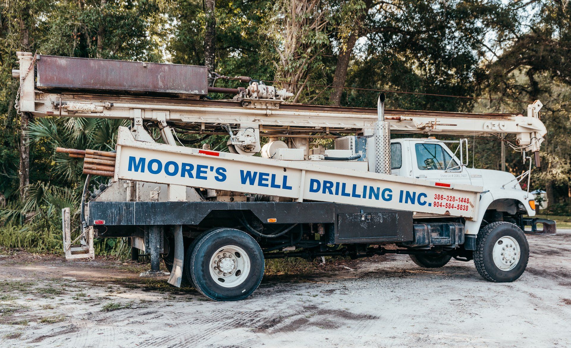 A Deep Well With A Bucket Full Of Water — Palatka, Fl — Moore’s Well Drilling White Moore's Well Drilling truck parked on a dirt road, drilling equipment visible, trees in the background.