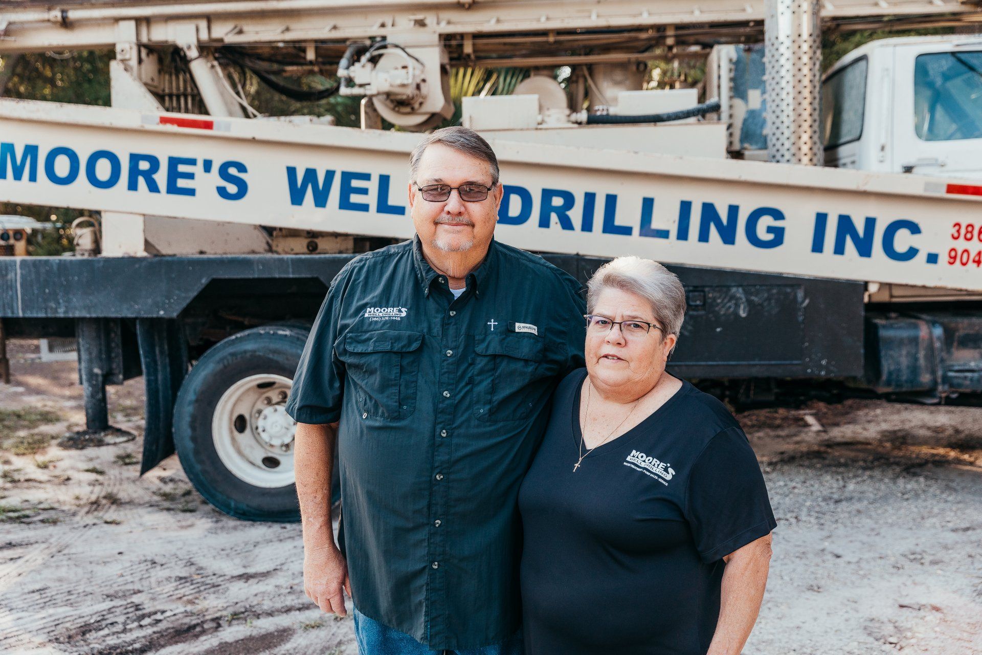 Moore Couple — Palatka, Fl — Moore’s Well Drilling Two people stand in front of a well drilling truck with company name and phone number.