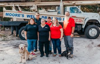 Group of people posing with dogs in front of a Moore's Well Drilling truck.