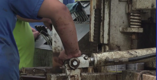 Well drilling crew operating drill rig controls during a water well installation.