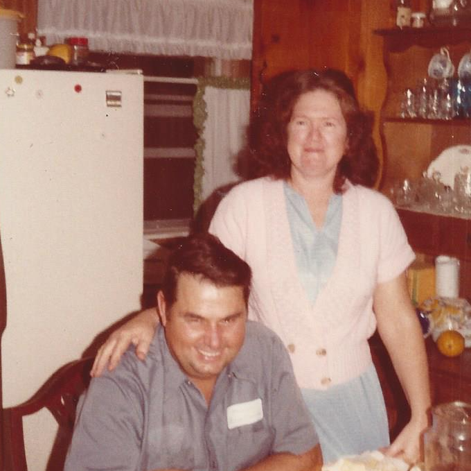 Old Picture Of A Man — Palatka, Fl — Moore’s Well Drilling Man sitting, woman standing behind, smiling in a kitchen; refrigerator, shelves with glassware visible.