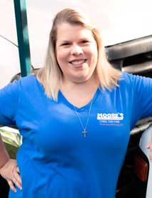 Woman wearing a blue shirt with a company logo smiling, outdoors, near a vehicle.