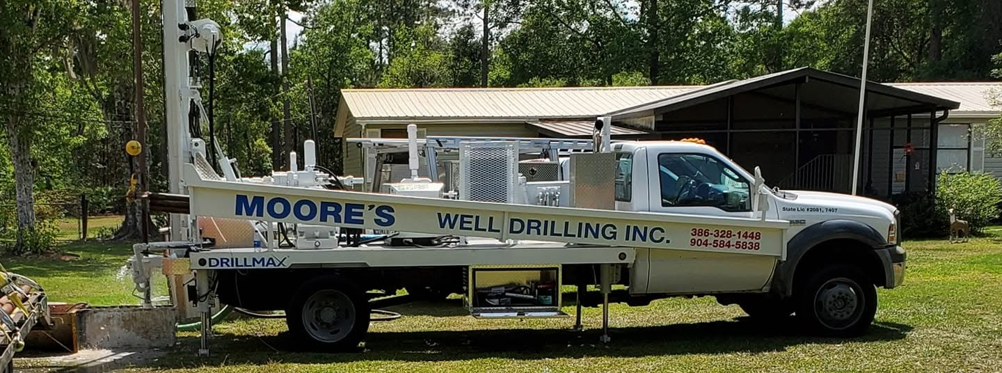 A Deep Well With A Bucket Full Of Water — Palatka, Fl — Moore’s Well Drilling White Moore's Well Drilling truck parked on a dirt road, drilling equipment visible, trees in the background.