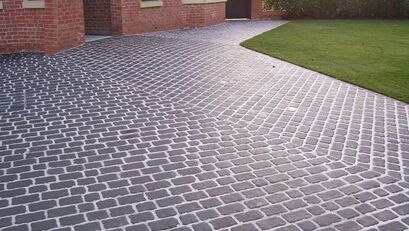 Wide driveway of grey cobbled paving curving round a lawn in Sheffield
