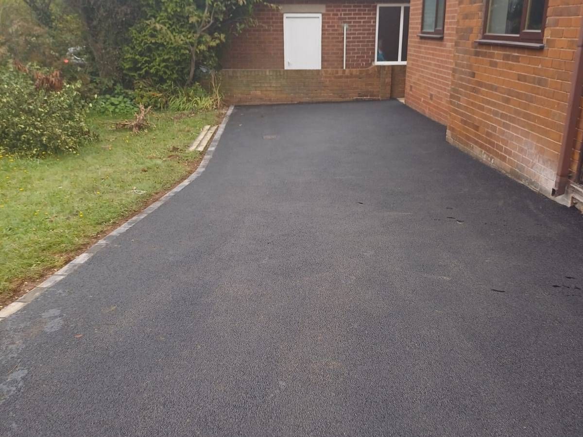 New black tarmac driveway with a grey kerb edge beside a lawn and brick house in Brampton, Sheffield