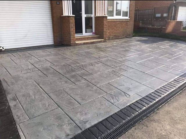 Grey slab-pattern imprinted concrete in front of a house with a channel drain