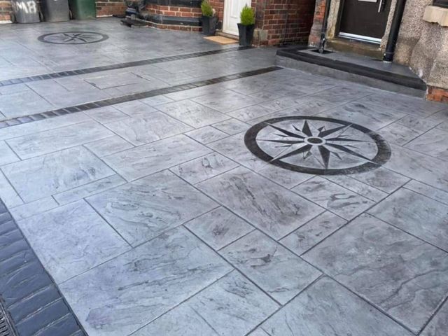 Grey slab-pattern imprinted concrete driveway with a dark compass star inset