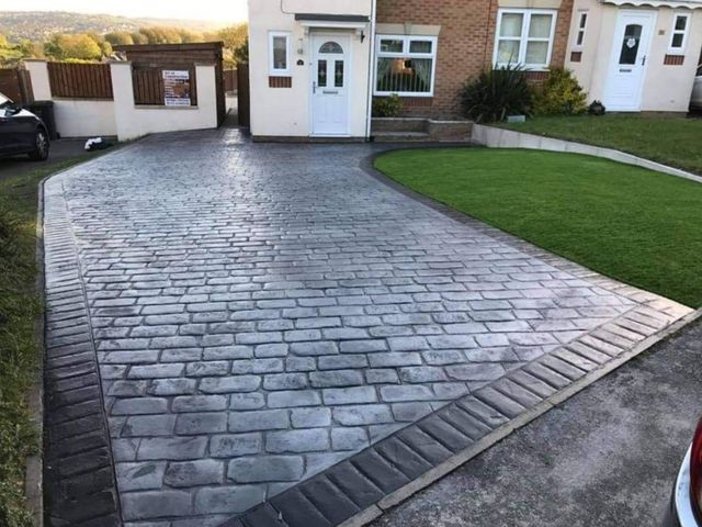 Grey cobble-pattern imprinted concrete driveway with a dark border in front of a house