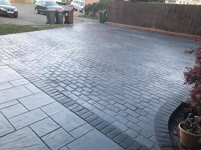 Charcoal cobble-pattern imprinted concrete driveway with a slab border