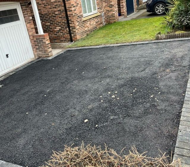 Worn black tarmac driveway in front of a garage in Sheffield before resurfacing