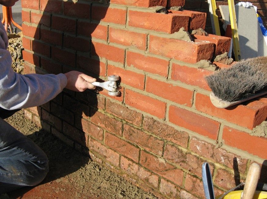Bricklayer pointing the joints of a new red brick garden wall in Sheffield