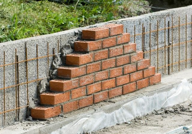 Red brick courses being built up against a reinforced block retaining wall in Sheffield