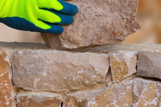 Gloved hand setting a stone into a new stone garden wall in Sheffield