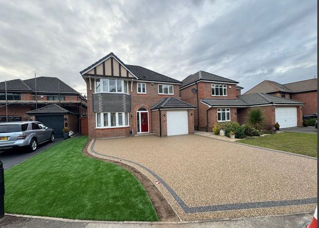 Resin driveway with a curved dark border leading up to a detached house and garage