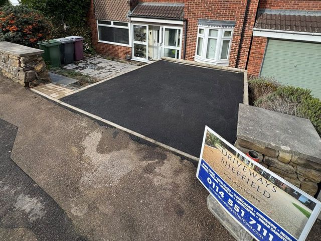 Black tarmac driveway with a buff block paving edge leading to the front door of a brick house in Dronfield