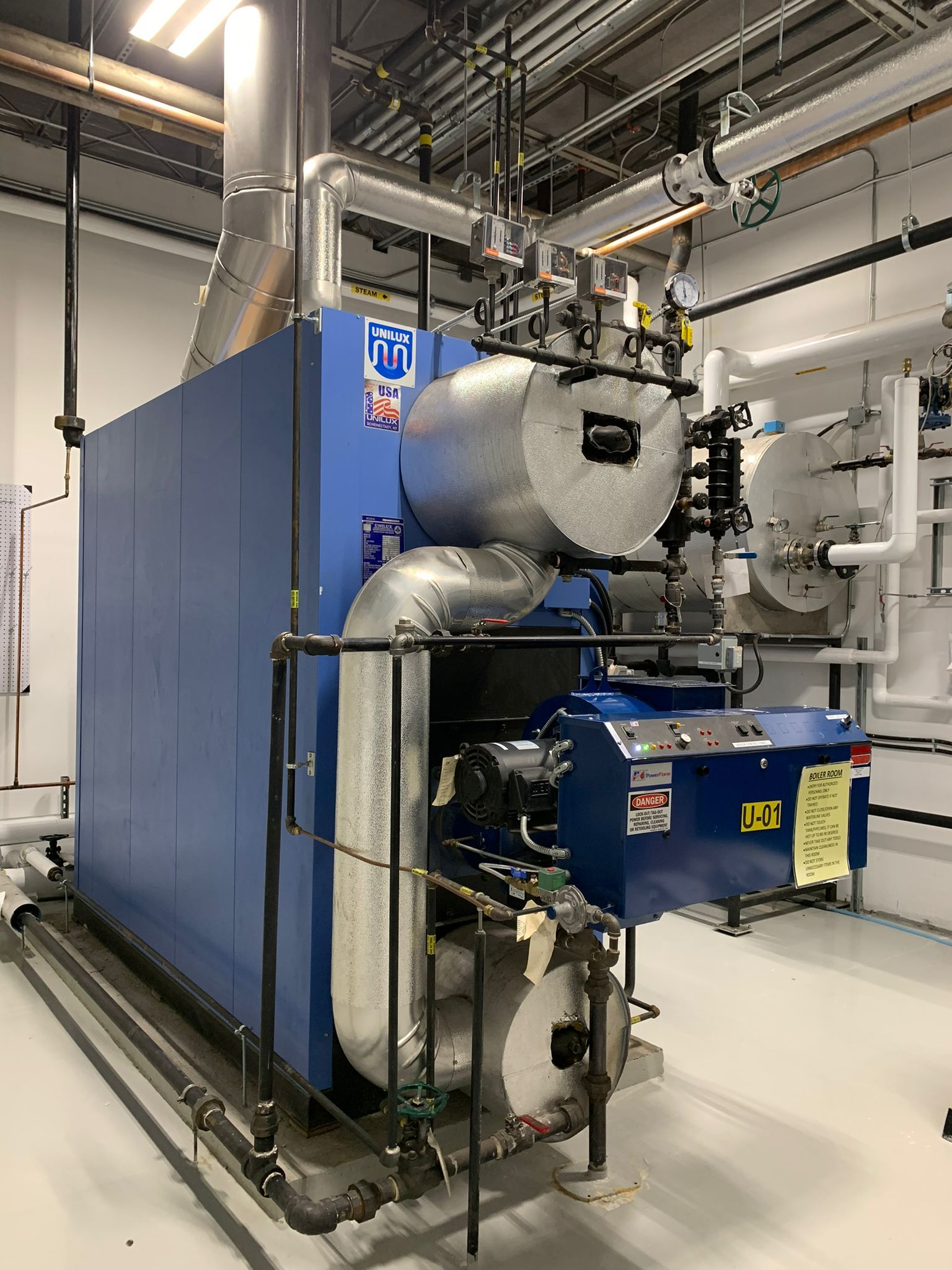 Blue industrial boiler in a utility room with metal piping.