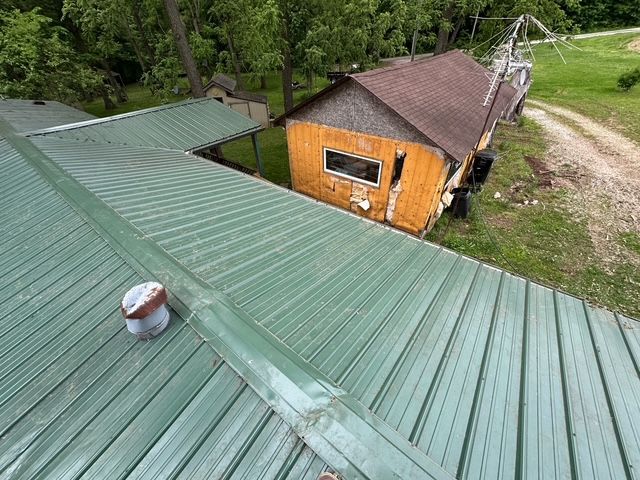 A high-angle view of a green metal roof adjacent to a structure with brown shingles and unfinished exterior walls.