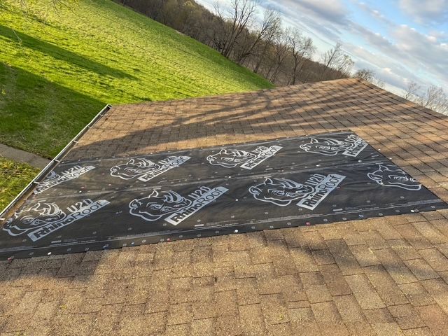 A patch of black synthetic roofing underlayment installed over brown asphalt shingles on a sloped residential roof.