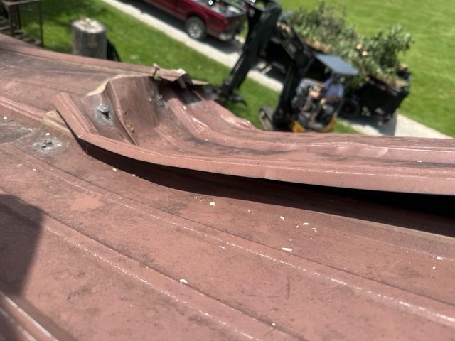 A damaged brown metal roof ridge cap with visible dents and bent sections, seen from a high angle.