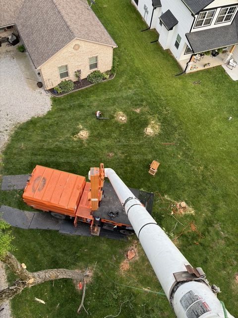 An aerial view of a residential lawn featuring a large orange wood chipper parked on protective mats.