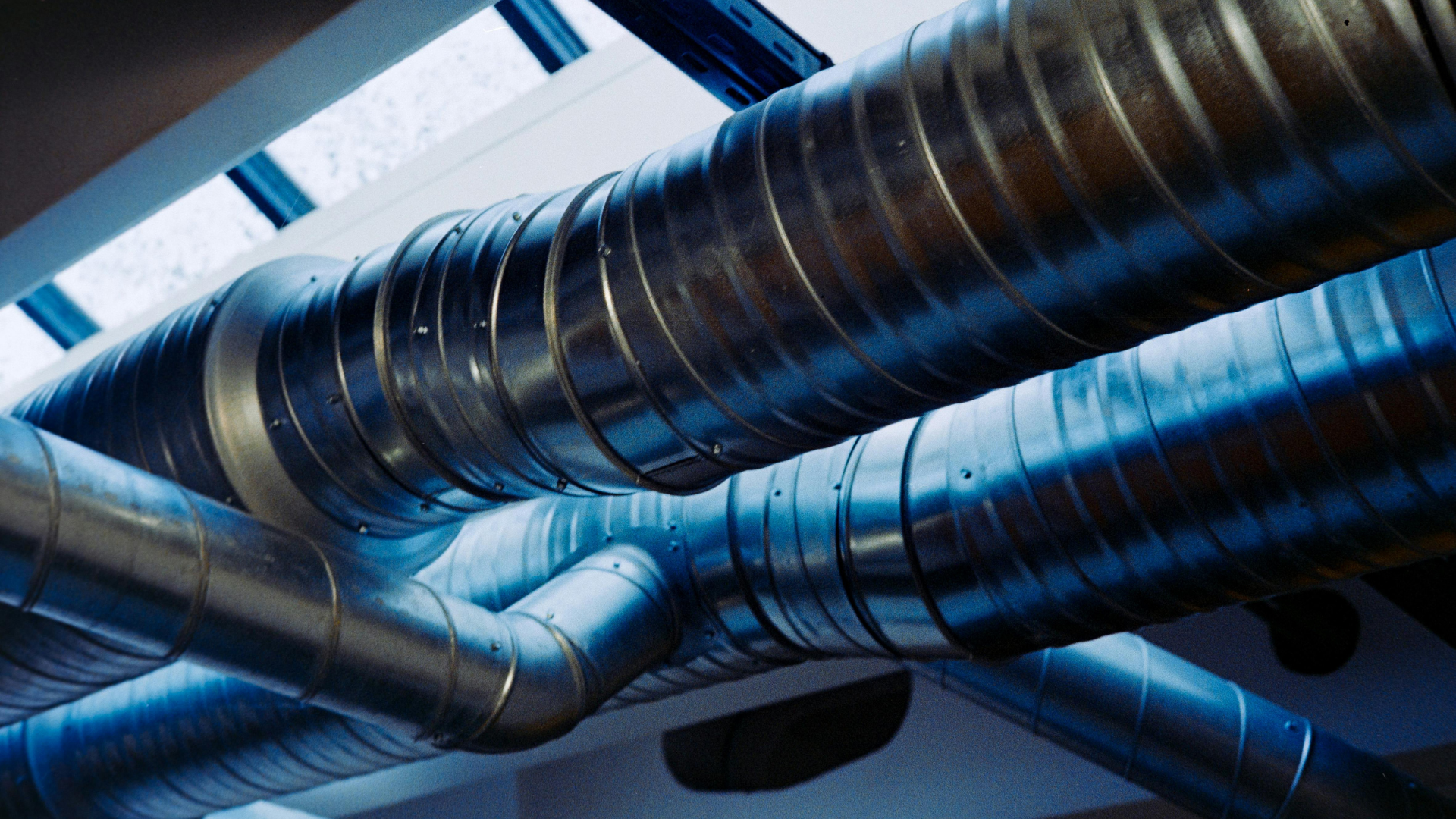 Metal ventilation ducts crossing beneath a blue-tinted industrial ceiling