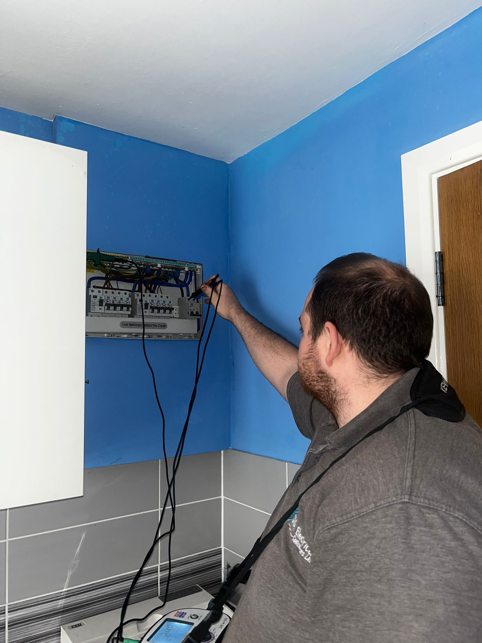 Man adjusting a wall-mounted device in a blue room with cables hanging down