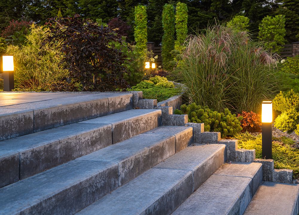 Stone steps lead up to a garden illuminated by amber lights at dusk.