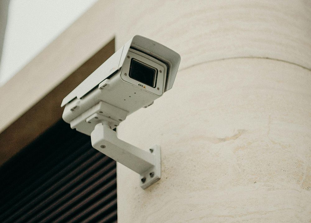 Security camera mounted on a cream-colored wall, angled slightly downwards.