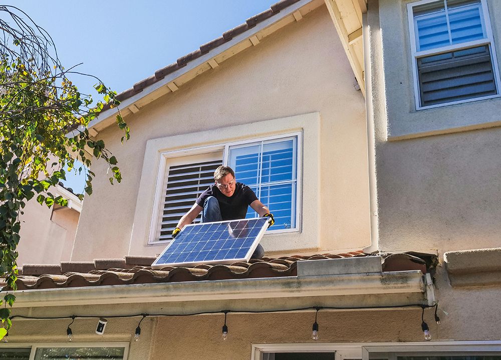 Man installing solar panel on a residential rooftop under a clear blue sky.