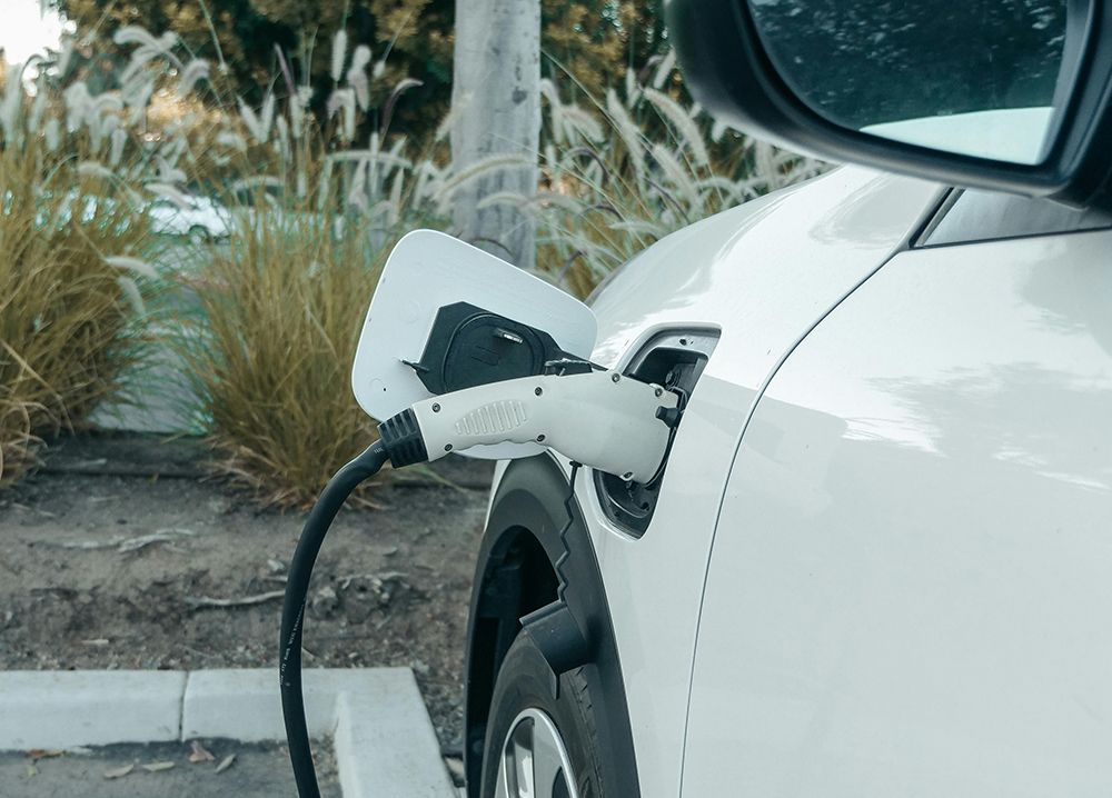 White electric car charging at a station outdoors; a charging cable is connected.