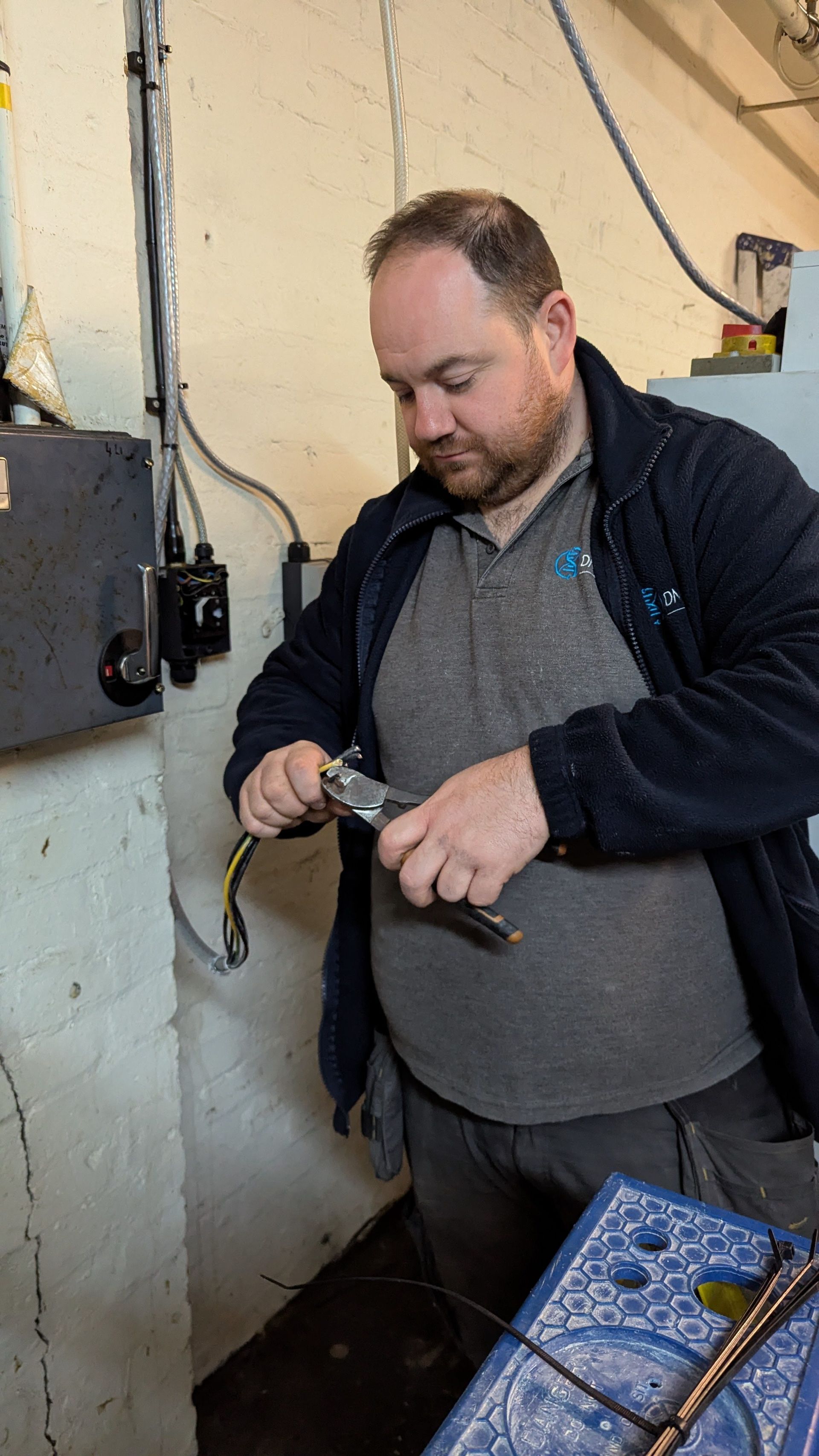Person adjusting a tool indoors beside a wall-mounted meter and wires