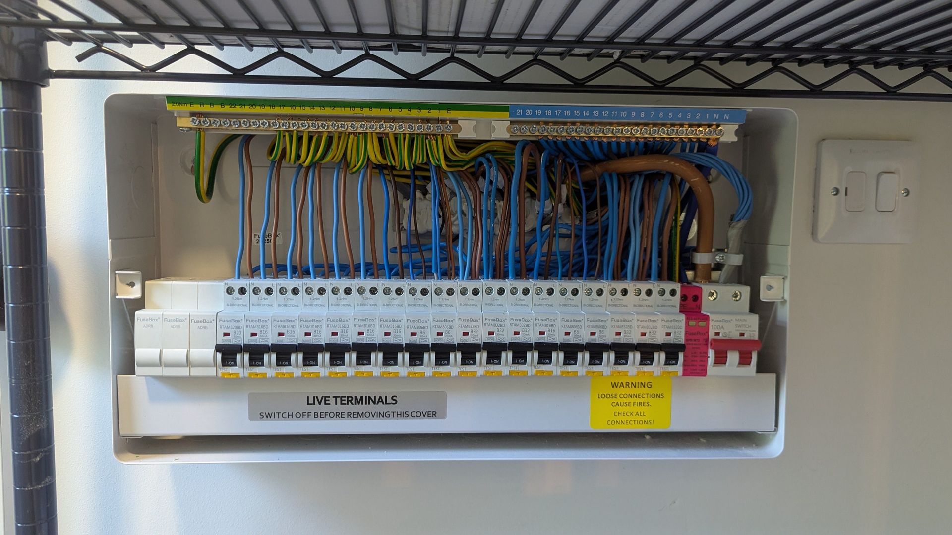 Electrical breaker panel with rows of switches and bundled colored wires inside a wall cabinet