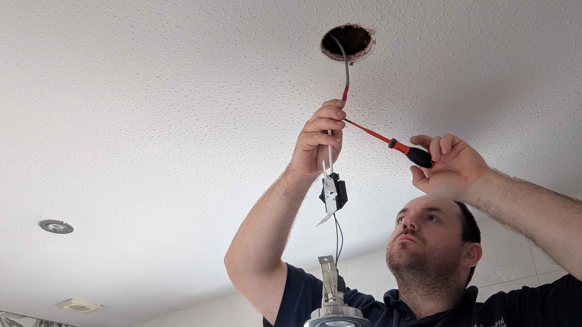 Man using screwdriver to connect wires to a ceiling light fixture in a white ceiling.