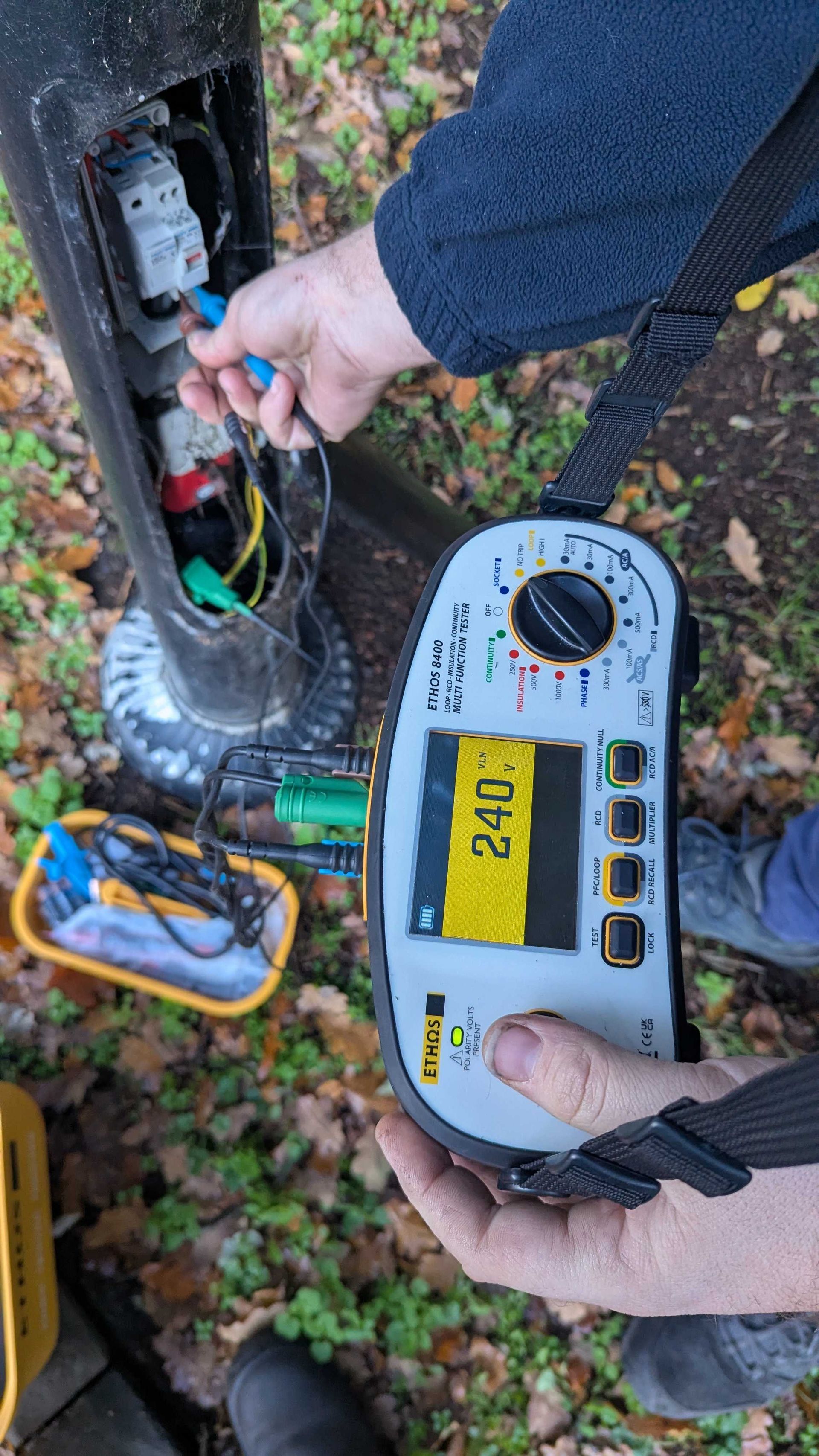 Person testing electrical wires inside a pole using a multimeter, displaying a reading of 240.