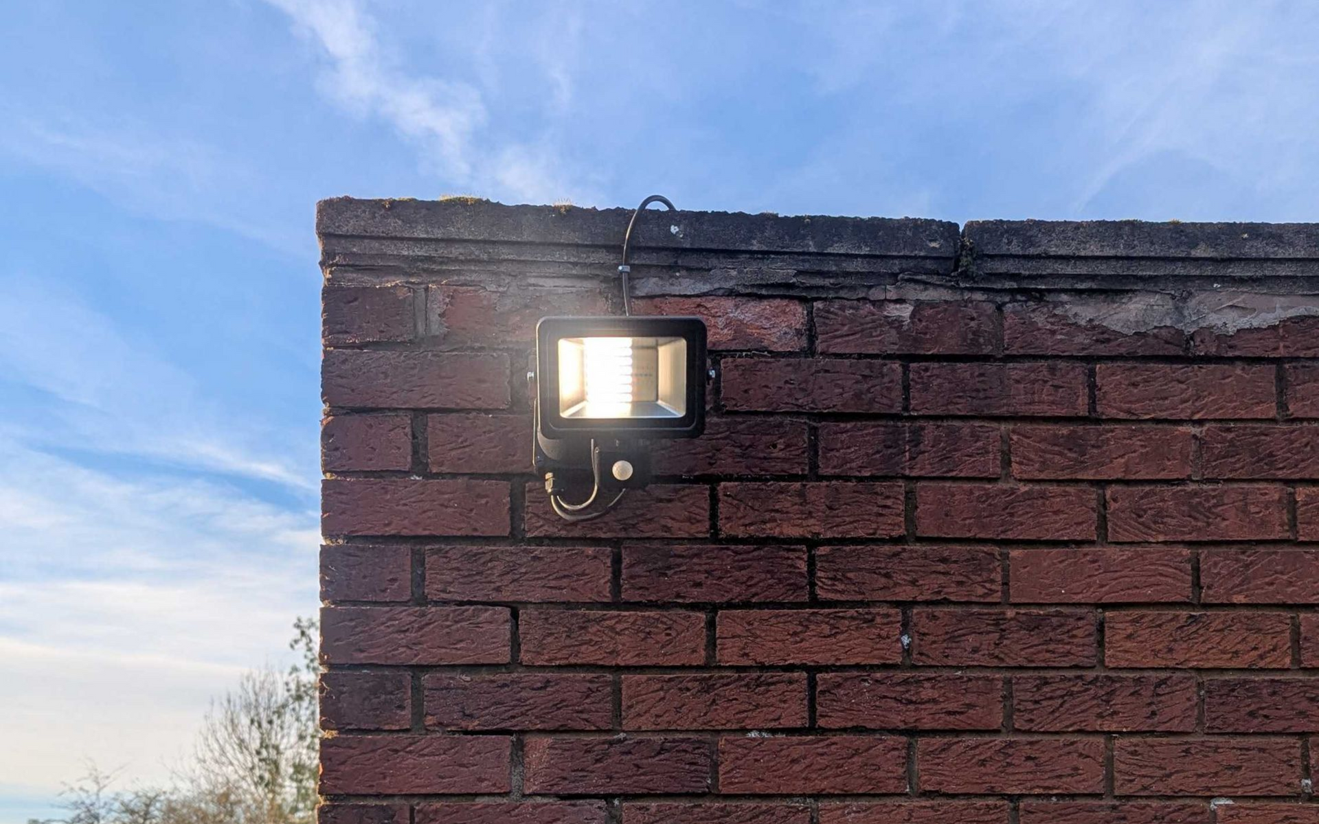 Bright floodlight on a brick wall corner, against a blue sky.