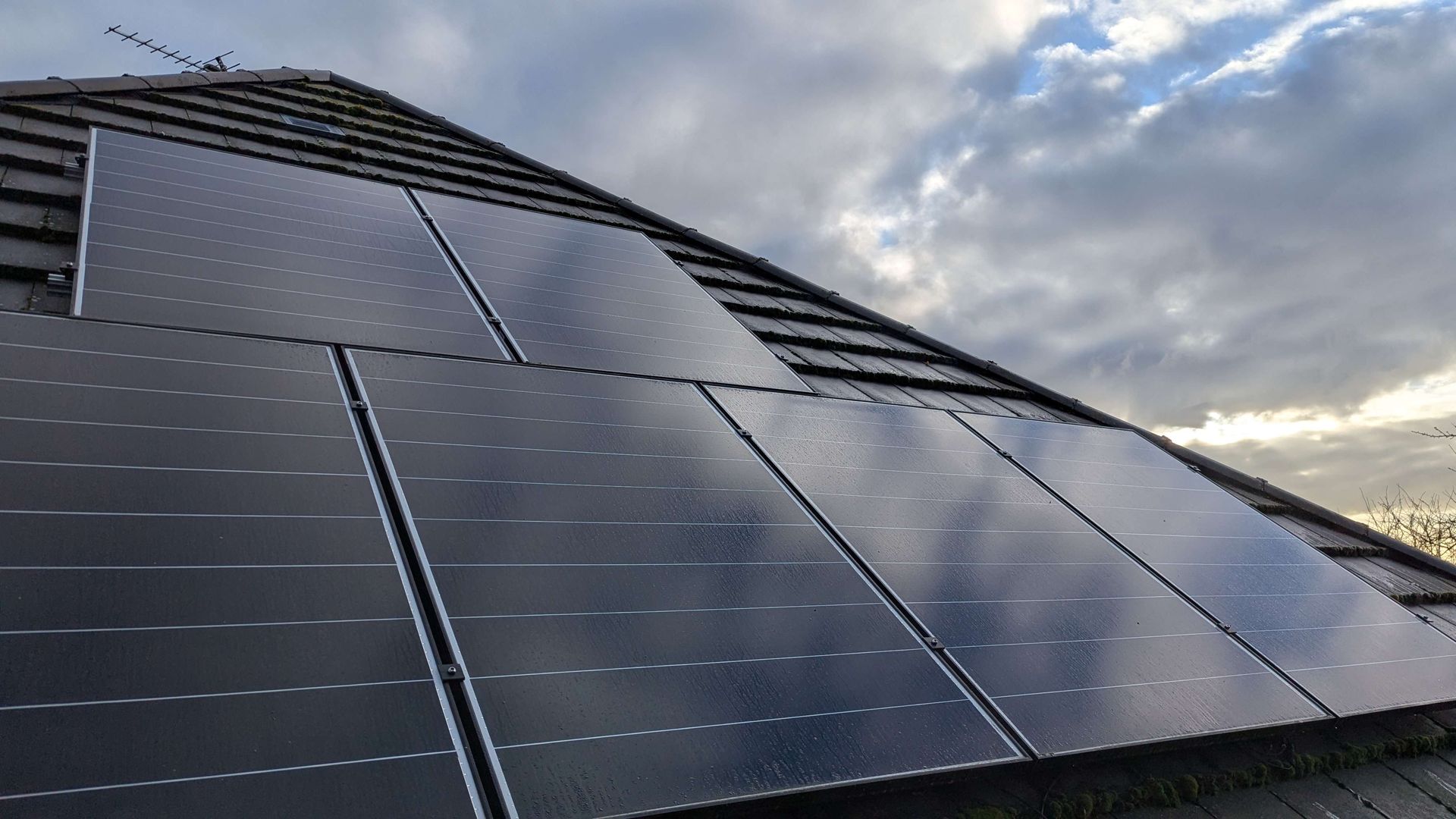 Solar panels on a tiled roof under a cloudy sky.