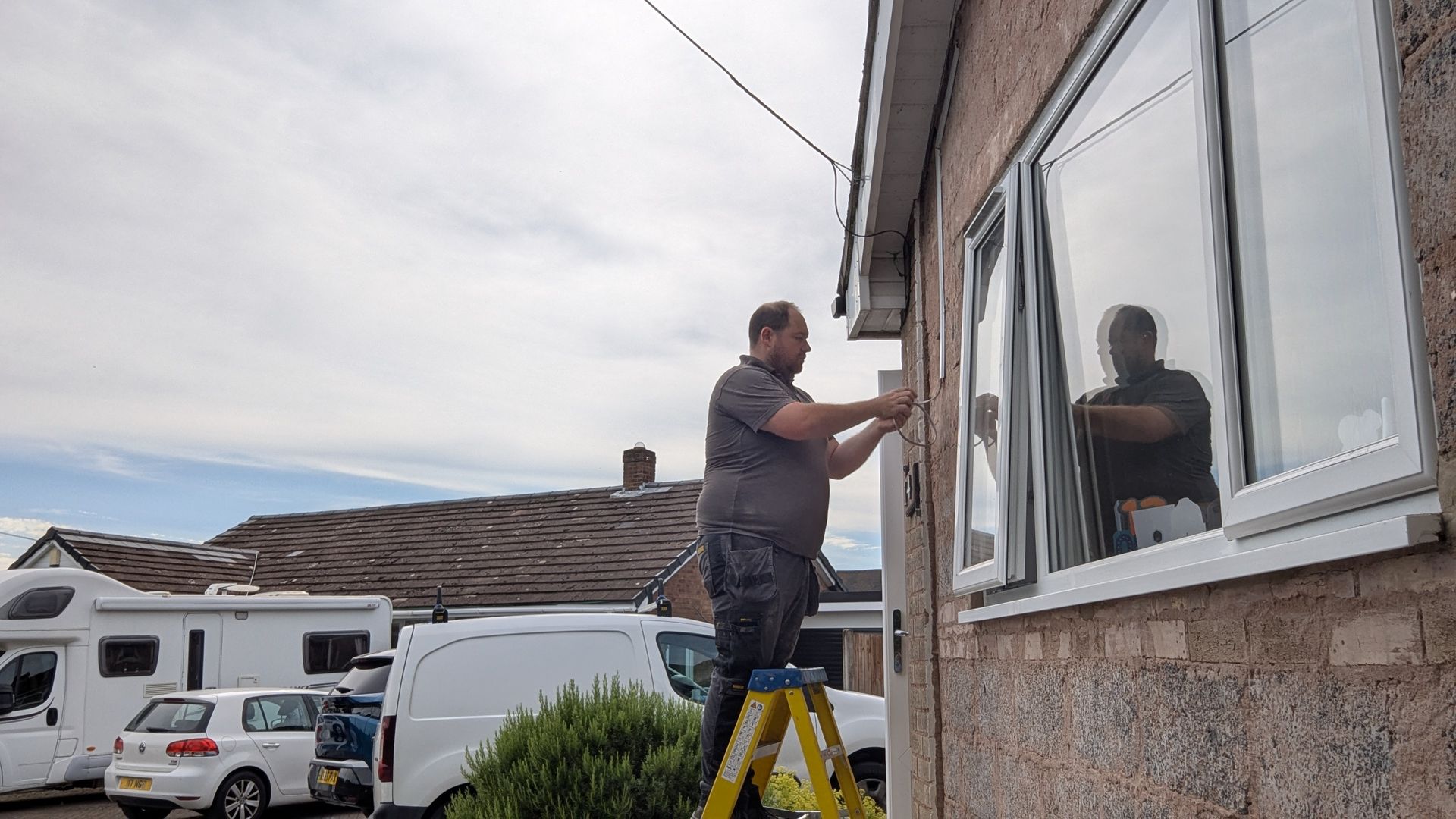 Man on a ladder installing security alarm or cctv