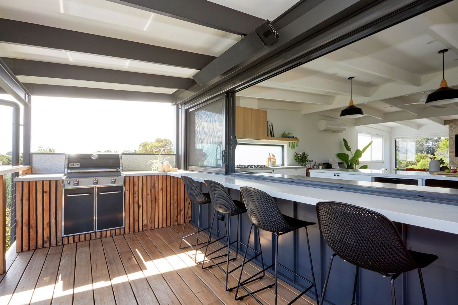 Outdoor kitchen with grill, bar seating, wooden deck, and open view.