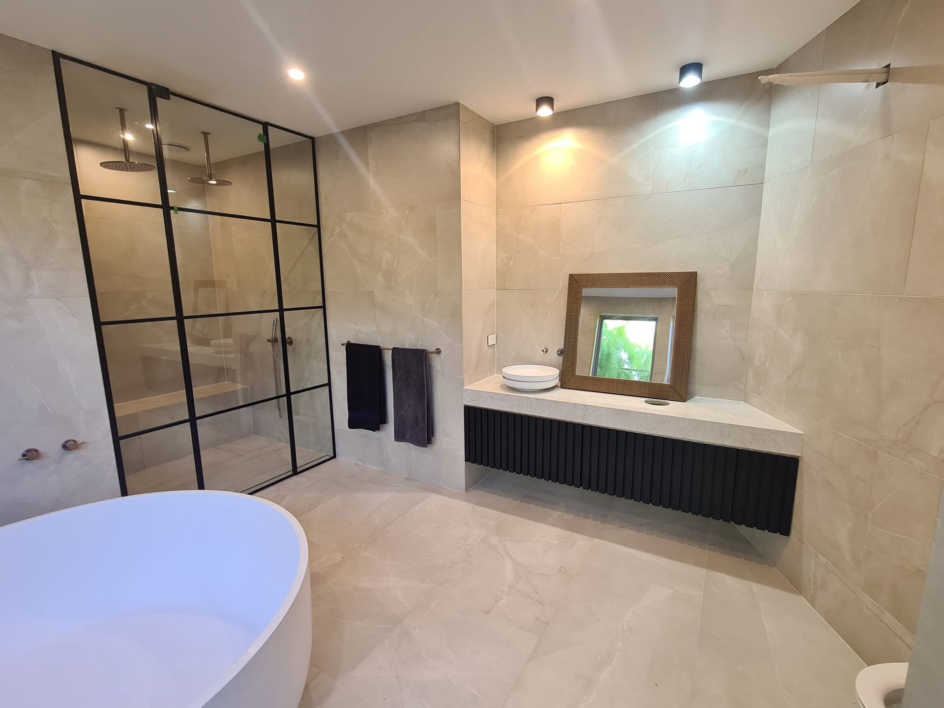 Modern bathroom with shower, tub, and vanity. Beige walls, black accents, and large window.
