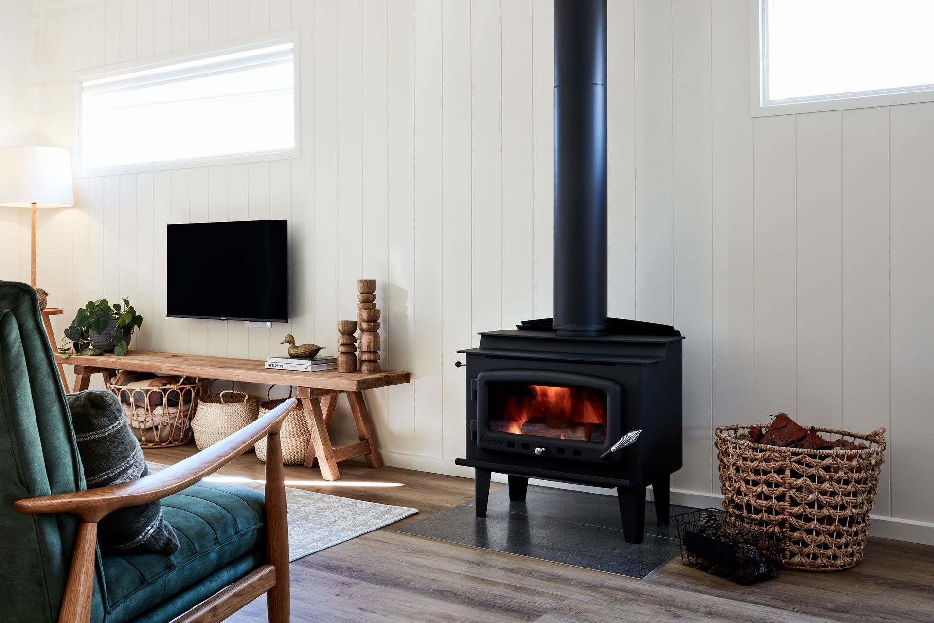 Cozy living room with a lit wood-burning stove, a green armchair, and a TV on the wall.