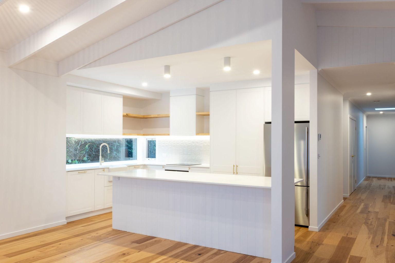 Modern white kitchen with island, stainless steel refrigerator, and wood floors.