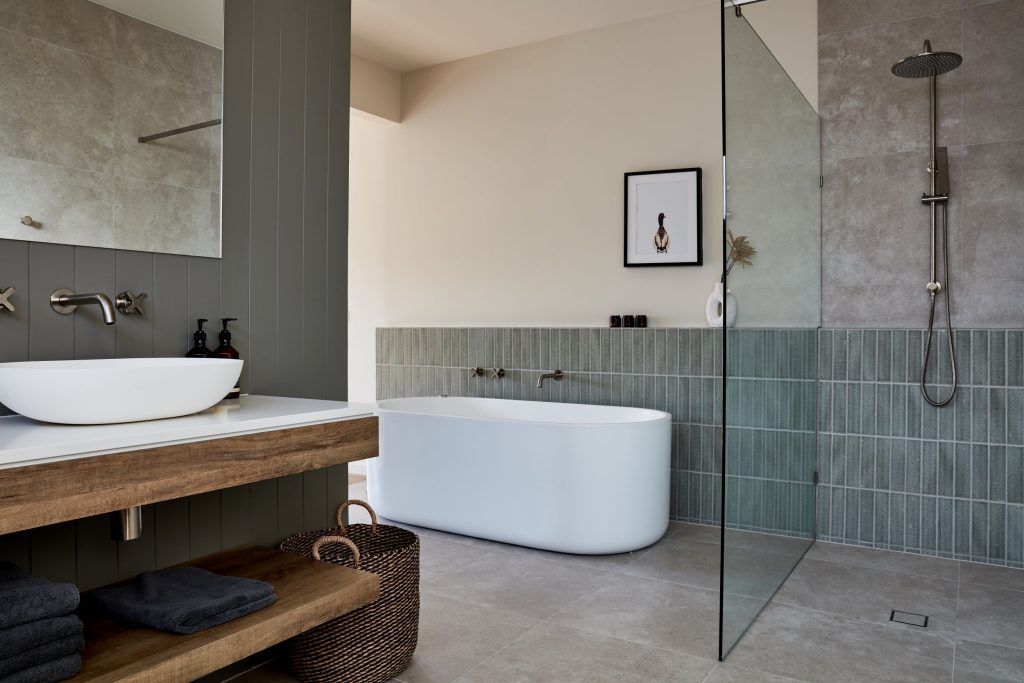 Bathroom with white bathtub, glass shower, wooden vanity, and gray walls.