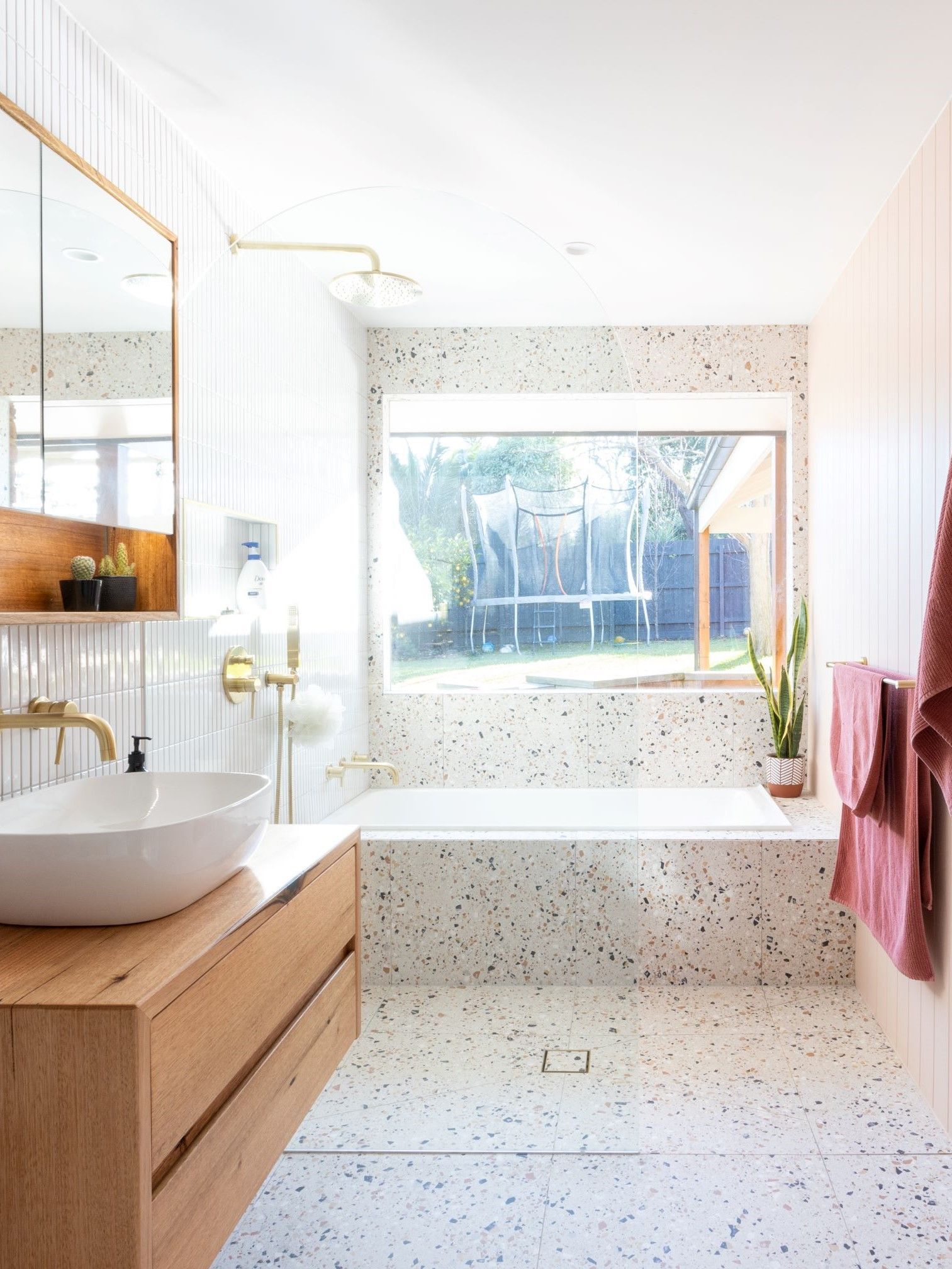 Modern bathroom with a wooden vanity, oval sink, terrazzo tile, bathtub, and window.