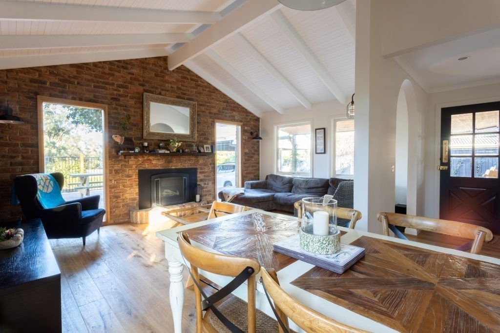 Living room with exposed brick fireplace, vaulted ceiling, and dining table.