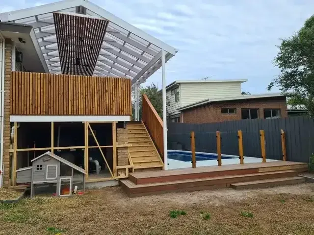 Backyard with a wooden deck, stairs, and a pool. A chicken coop sits nearby. Overcast sky.