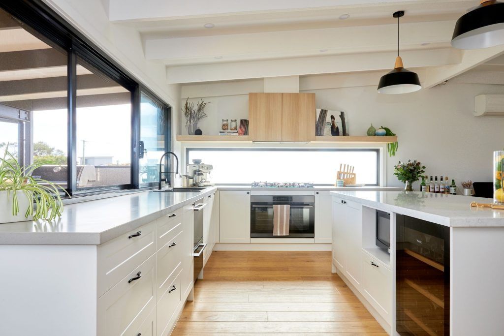 Modern kitchen with white cabinets, stainless steel appliances, and large windows.